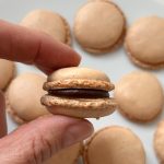 Hand hält gefülltes Macaron mit Schokoladenganache über weiterem Gebäck