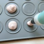 Rosa Macaron-Masse wird mit Spritzbeutel auf Silikonmatte gespritzt