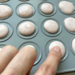 Rosa Macaron-Schalen in Silikonform, Finger prüft Kruste vor dem Backen