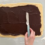 Schokoladenfüllung wird mit Winkelpalette auf ausgerolltem Hefeteig gestrichen