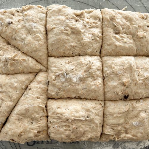 Bemehlter Brötchenteig in gleichmäßige Quadrate geschnitten auf Backmatte