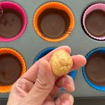 Erdnussbutterkugel über bunten Silikonförmchen mit geschmolzener Schokolade
