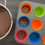 Geschmolzene Schokolade wird in bunte Silikonförmchen im Muffinblech gefüllt