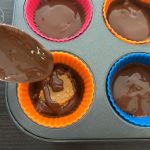 Geschmolzene Schokolade wird über Erdnussbutterfüllung in Silikonförmchen gegossen