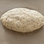 Ungebackener Brotlaib aus Vollkornteig mit Hüttenkäse auf Backpapier geformt