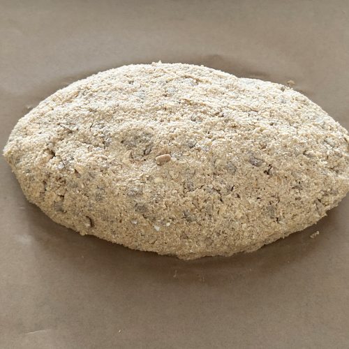Ungebackener Brotlaib aus Vollkornteig mit Hüttenkäse auf Backpapier geformt