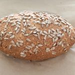 Ovales Proteinbrot mit Hüttenkäse, dicht mit Sonnenblumenkernen bestreut, auf Backpapier