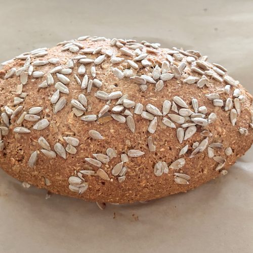 Ovales Proteinbrot mit Hüttenkäse, dicht mit Sonnenblumenkernen bestreut, auf Backpapier